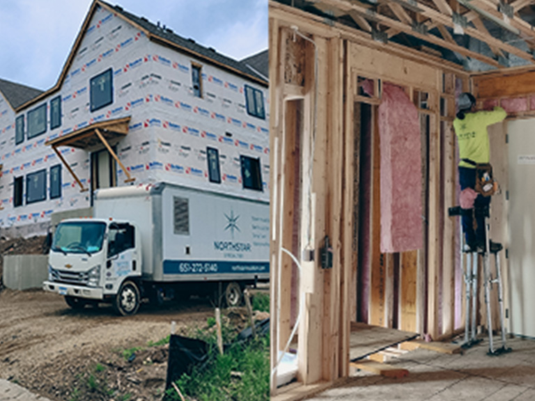 A professional installer on stilts fitting pink fiberglass batt insulation into the wall framing of a new residential home construction site in Minnesota.