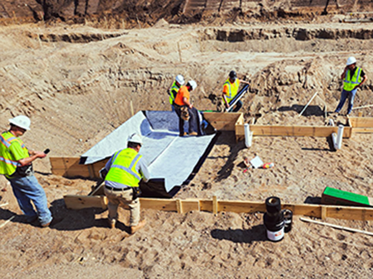 Construction crew installing commercial exterior waterproofing membranes for an elevator pit foundation at a new building site in Minnesota.