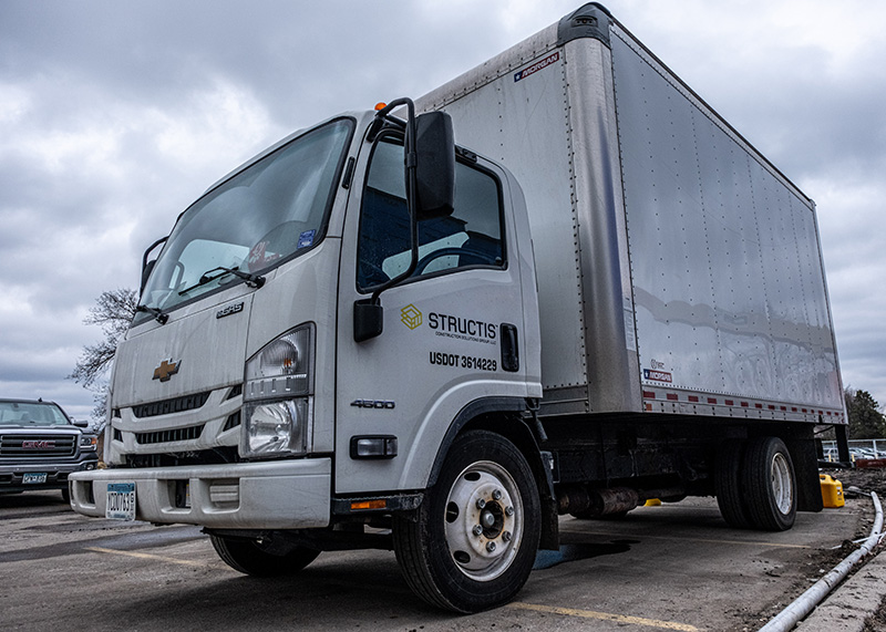 A branded Structis commercial box truck parked on a concrete job site during an insulation and air barrier project in Minnesota.