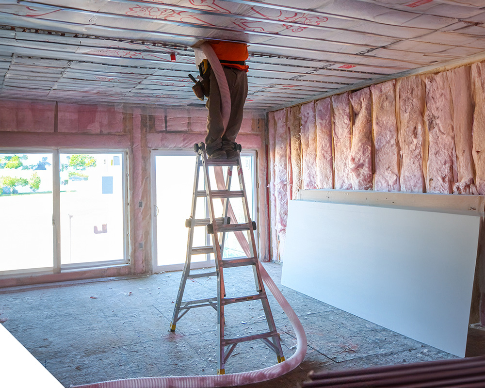 Structis insulation contractor on a stepladder blowing loose-fill insulation into a ceiling cavity in a Minnesota building.